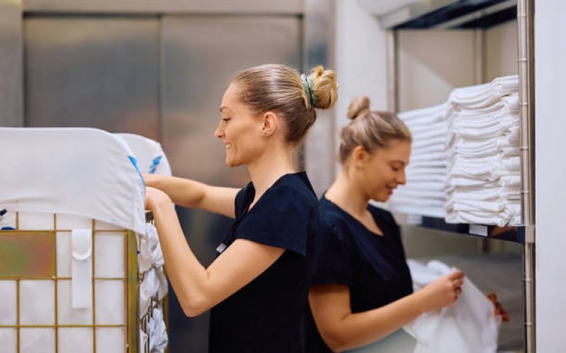 Happy housekeeper and her coworker sorting clean linens in hotel laundry room.